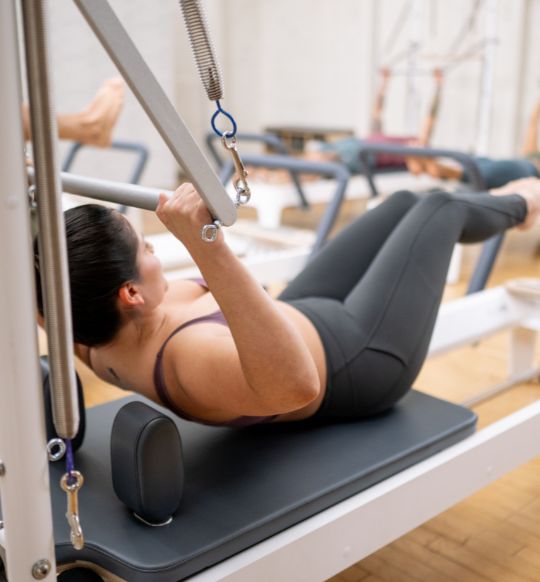 Person performing Pilates exercise on reformer machine in studio.