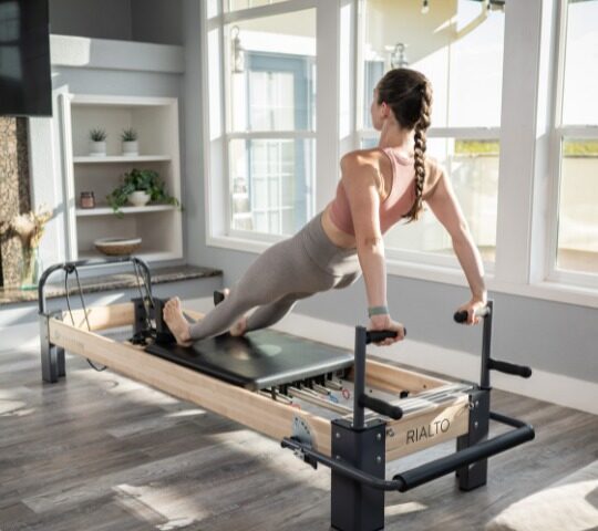 Pilates studio equipment setup with a woman using a reformer.