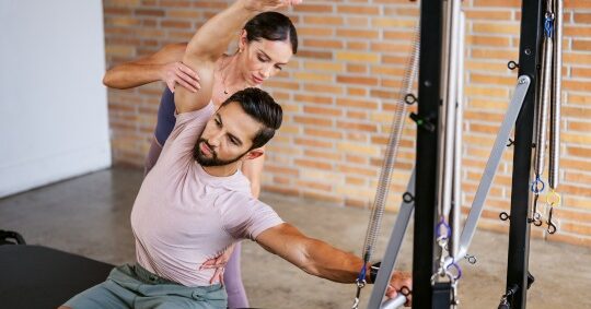 Pilates instructor guiding student with professional equipment.