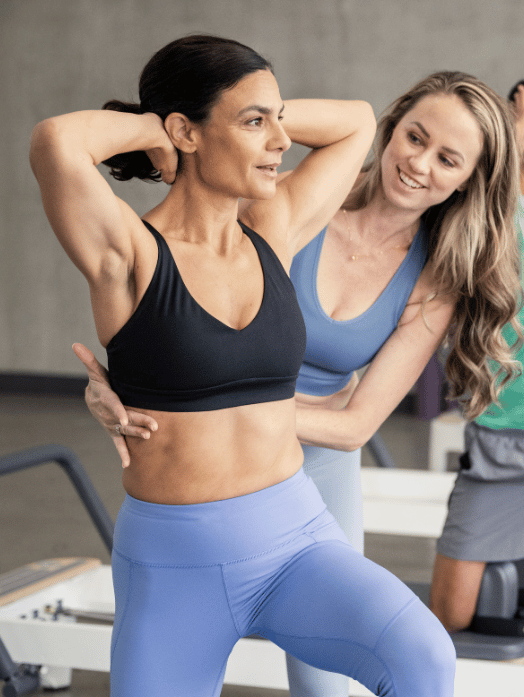Pilates instructor guiding student on reformer in studio setting.